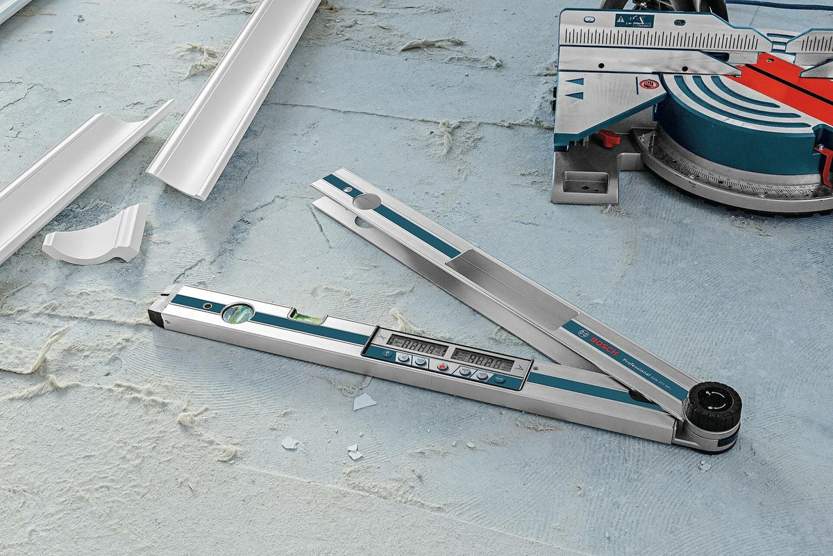 A close-up of the Bosch GAM 270 MFL on a dusty floor, displaying an angle measurement, with pieces of cut crown molding and a miter saw in the background.