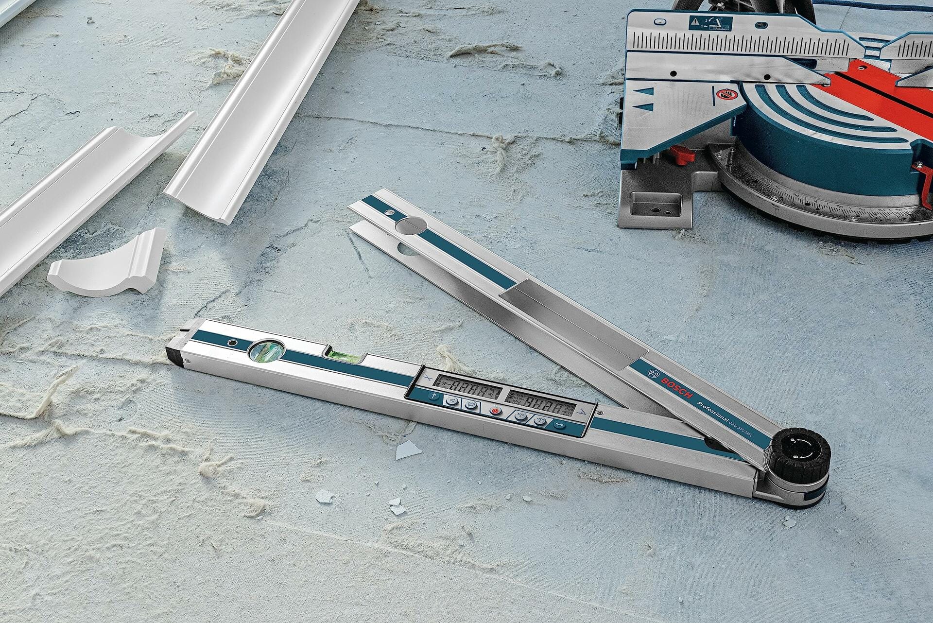 A close-up of the Bosch GAM 270 MFL on a dusty floor, displaying an angle measurement, with pieces of cut crown molding and a miter saw in the background.