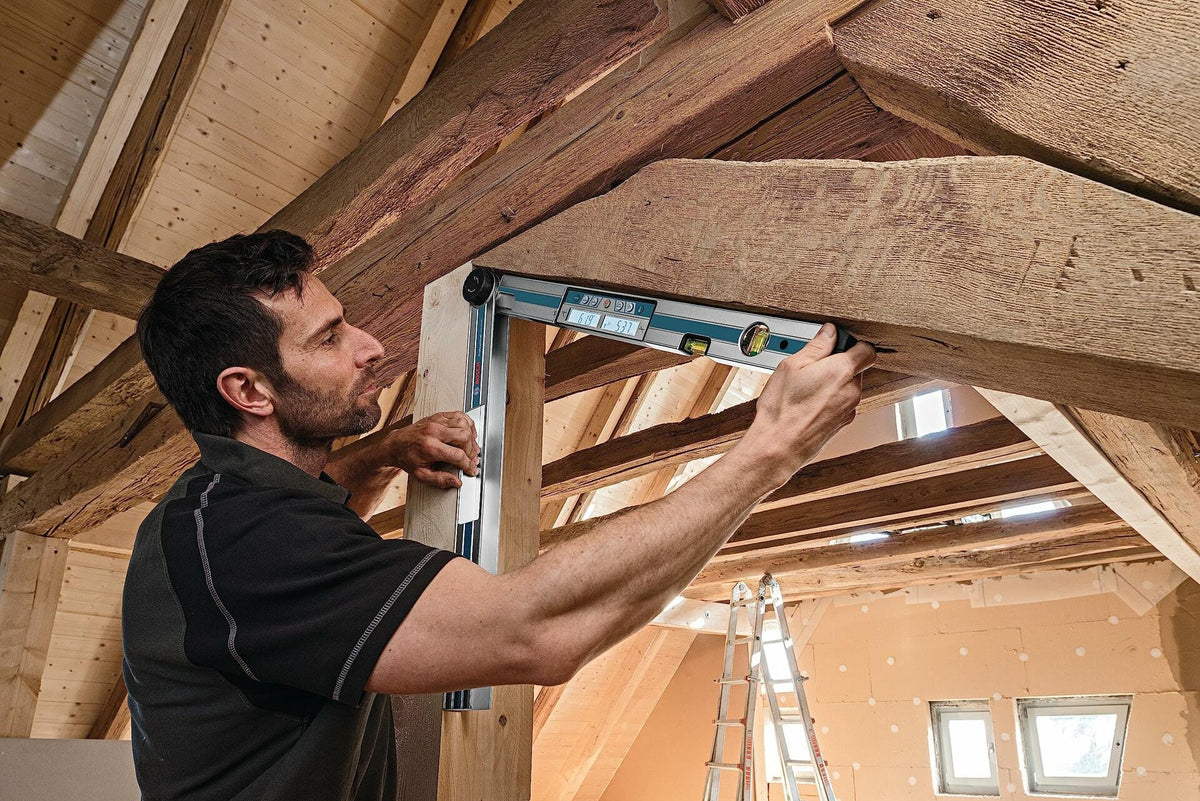 A carpenter uses the Bosch GAM 270 MFL to measure the complex angle between a vertical post and a large, rustic wooden ceiling beam in a framing application.