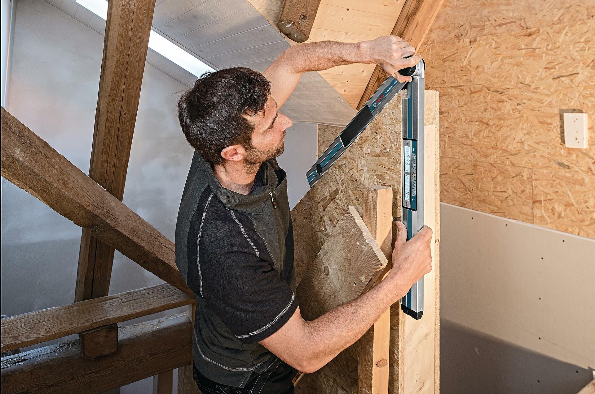 A carpenter holds the Bosch digital angle finder vertically against a wooden structure to measure and verify an angle, demonstrating its use in framing and construction.