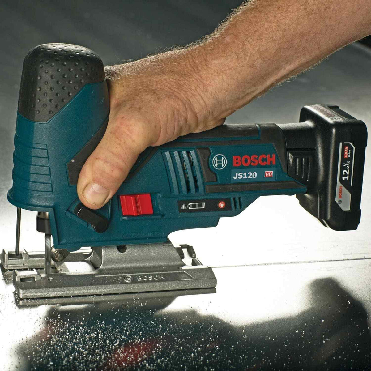 A close-up action shot of a person using a Bosch JS120 jigsaw powered by a 12V battery to cut through a metal surface.