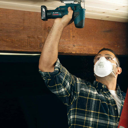 Action shot of a professional wearing a dust mask and safety goggles while using a cordless Bosch 12V Max jigsaw for an overhead wood cutting application.