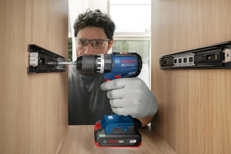 An industrial installer utilizing a Bosch compact cordless drill powered by an 18V 2.0Ah replacement battery pack to align and screw steel slider tracks inside a custom wooden drawer housing assembly. This graphic-free action variant emphasizes the agile maneuverability of the slim lithium-ion pack during intricate internal cabinet carpentry work.