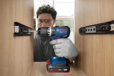An industrial installer utilizing a Bosch compact cordless drill powered by an 18V 2.0Ah replacement battery pack to align and screw steel slider tracks inside a custom wooden drawer housing assembly. This graphic-free action variant emphasizes the agile maneuverability of the slim lithium-ion pack during intricate internal cabinet carpentry work.