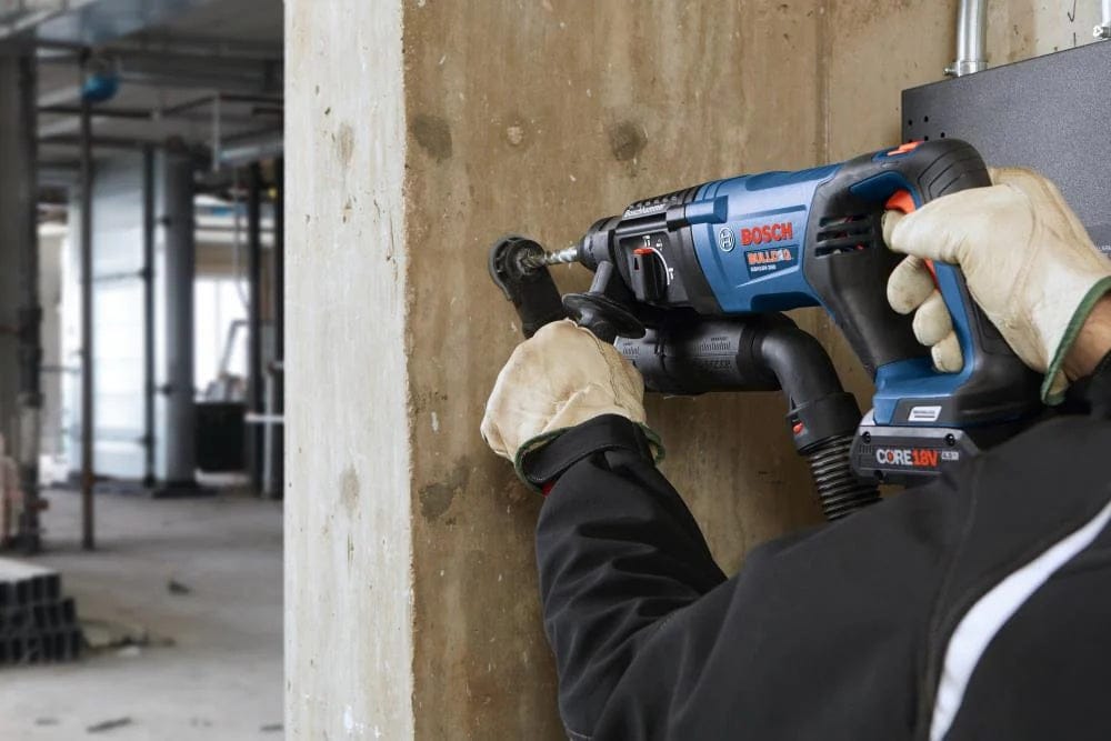 A worker using the Bosch 18V brushless 1-inch SDS-Plus Bulldog rotary hammer to drill into a reinforced concrete pillar in an industrial building interior.