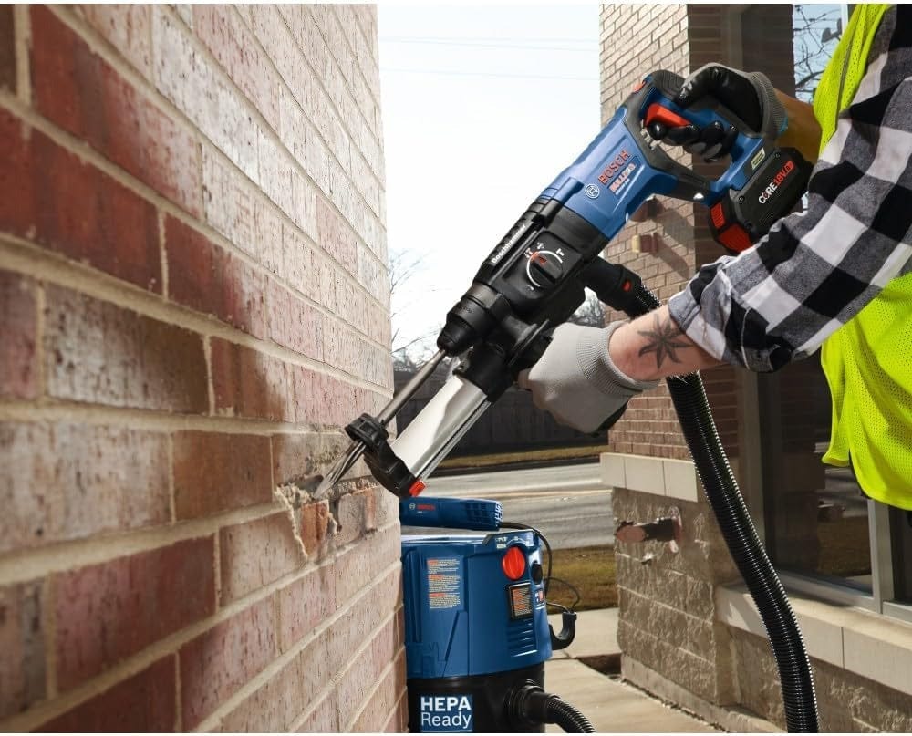 A close-up view of a worker using the Bosch SDS-Plus Bulldog rotary hammer and a HEPA-ready vacuum attachment to perform clean, dustless drilling into an exterior brick wall.