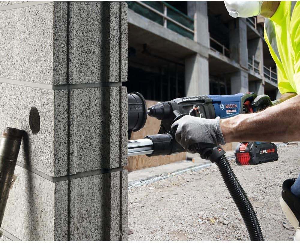 A construction worker utilizing the Bosch 18V cordless Bulldog rotary hammer and a dust collection shroud to drill precise large-diameter holes into a structural concrete block wall.