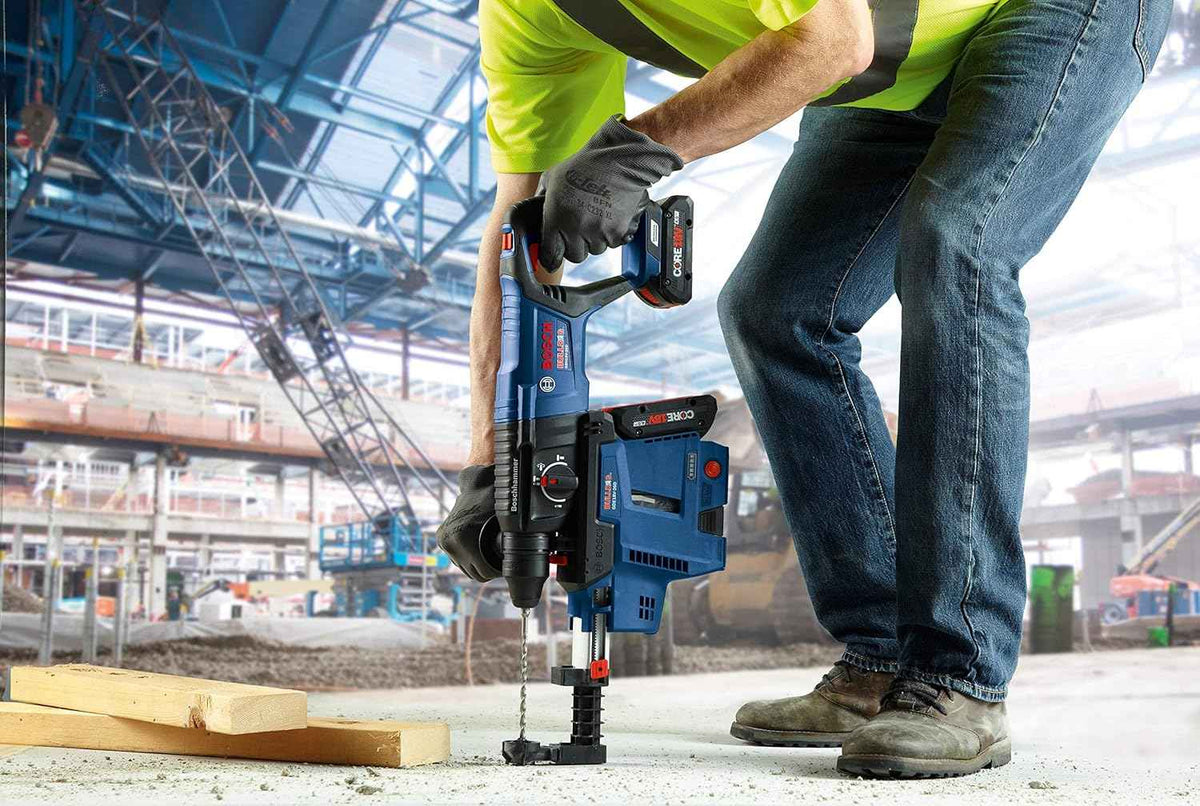 An on-site action shot of a professional using the Bosch GBH18V-26D rotary hammer with a GDE18V-16 integrated dust extraction system to drill downward into a concrete floor slab.