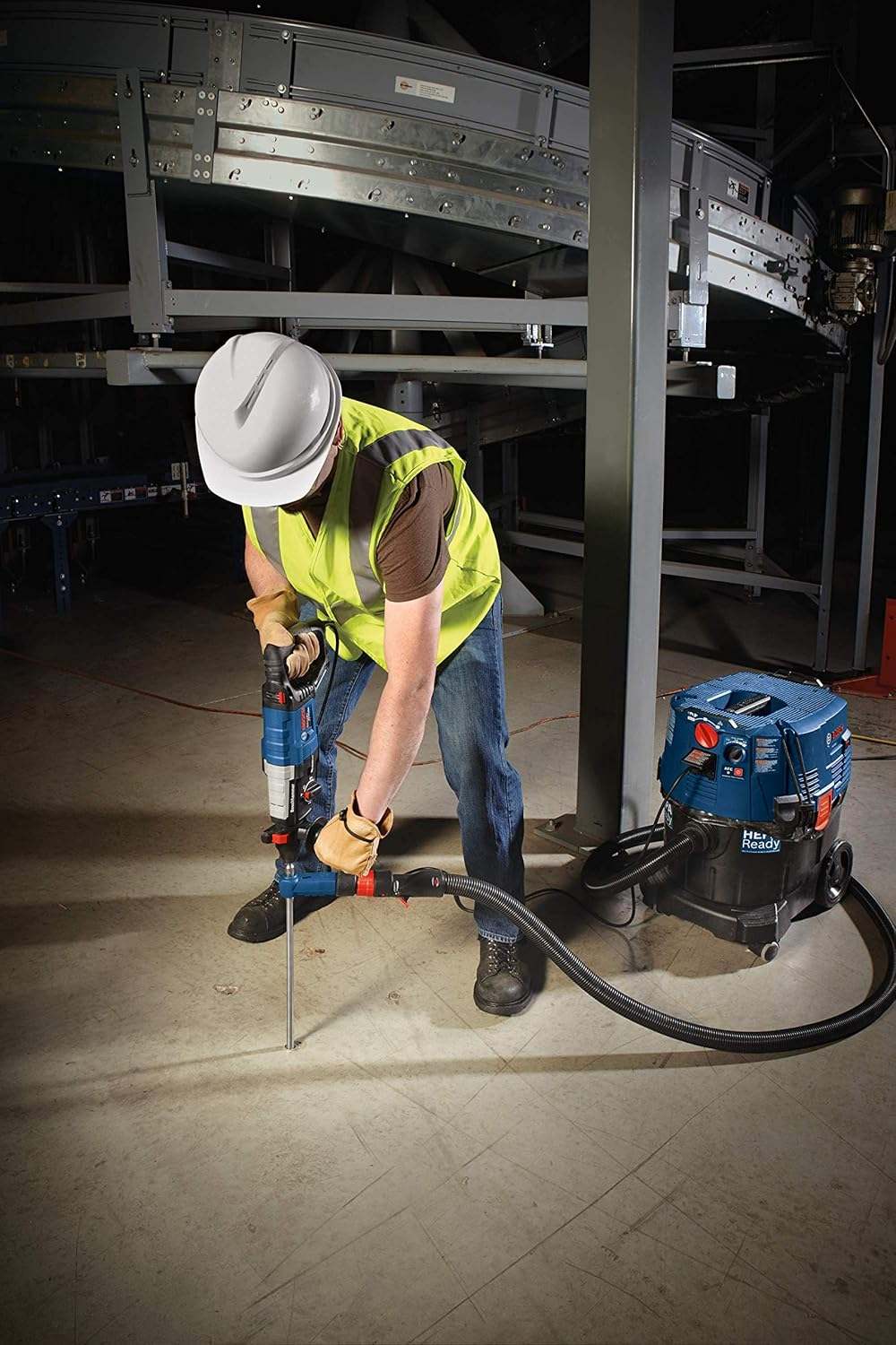An operative using the Bosch GBH2-28L-RT and a connected dust extractor to drill a vertical hole into a concrete floor in a large commercial facility.