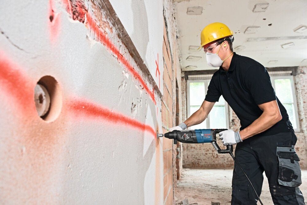 A worker using the Bosch Bulldog rotary hammer to drill into a brick and plaster wall, following a red laser layout line for accurate placement.