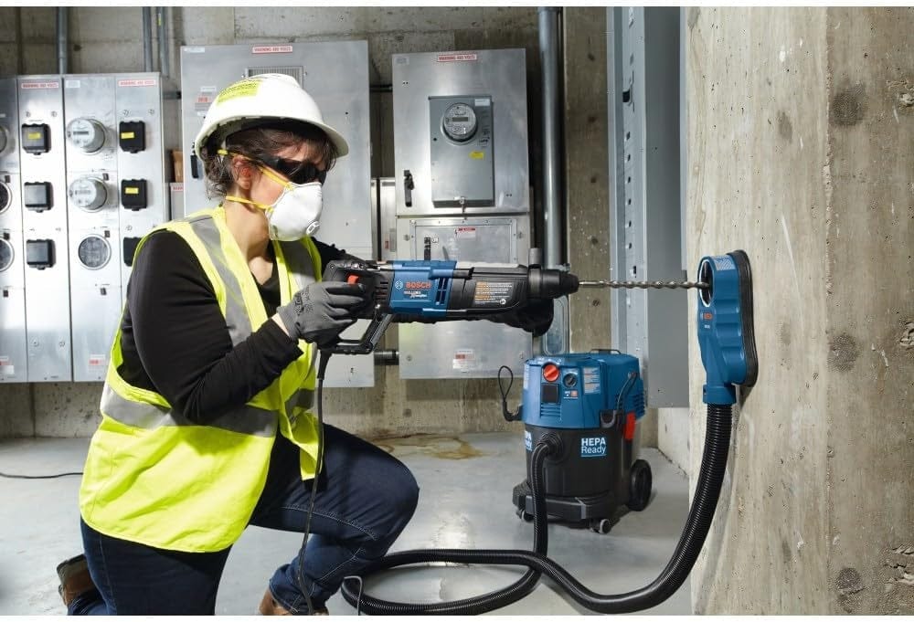 A technician in safety gear using the Bosch GBH2-28L-RT rotary hammer with a dust extraction attachment to drill into a concrete wall.