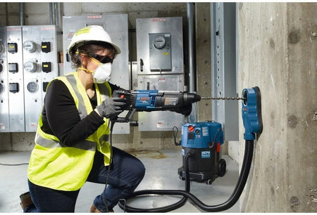 A technician in safety gear using the Bosch GBH2-28L-RT rotary hammer with a dust extraction attachment to drill into a concrete wall.
