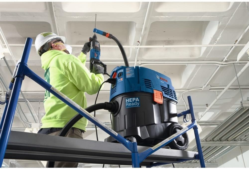 Construction professional using the Bosch 1-1/8 inch Bulldog rotary hammer for overhead concrete drilling while integrated with a HEPA-ready dust extractor system.