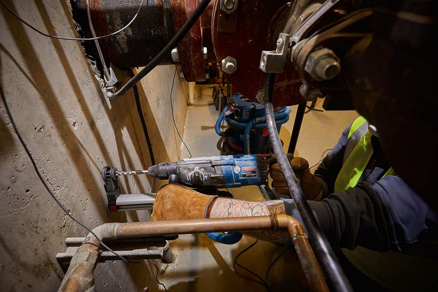 Close-up action shot of a worker using the Bosch GBH2-28L-RT rotary hammer to drill into a thick concrete wall in a industrial environment.