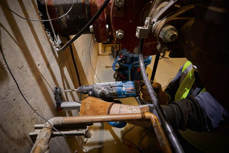 Close-up action shot of a worker using the Bosch GBH2-28L-RT rotary hammer to drill into a thick concrete wall in a industrial environment.