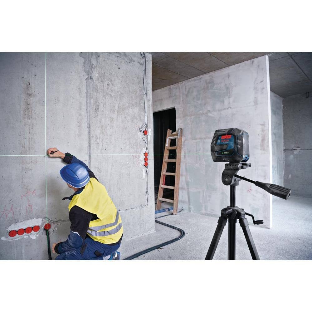 An application photo of the Bosch GCL100-40G mounted on a tripod in a construction setting, where a professional contractor is using the projected green laser lines to accurately mark layout points on a concrete wall.