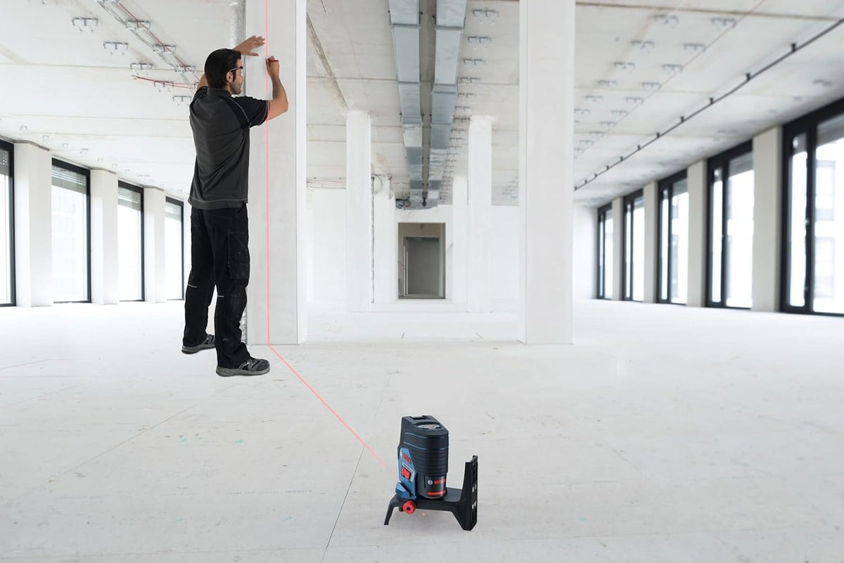 An action shot of a professional using the Bosch GCL100-80C-RT in a construction space, projecting a vertical red plumb line onto a column for precise alignment.