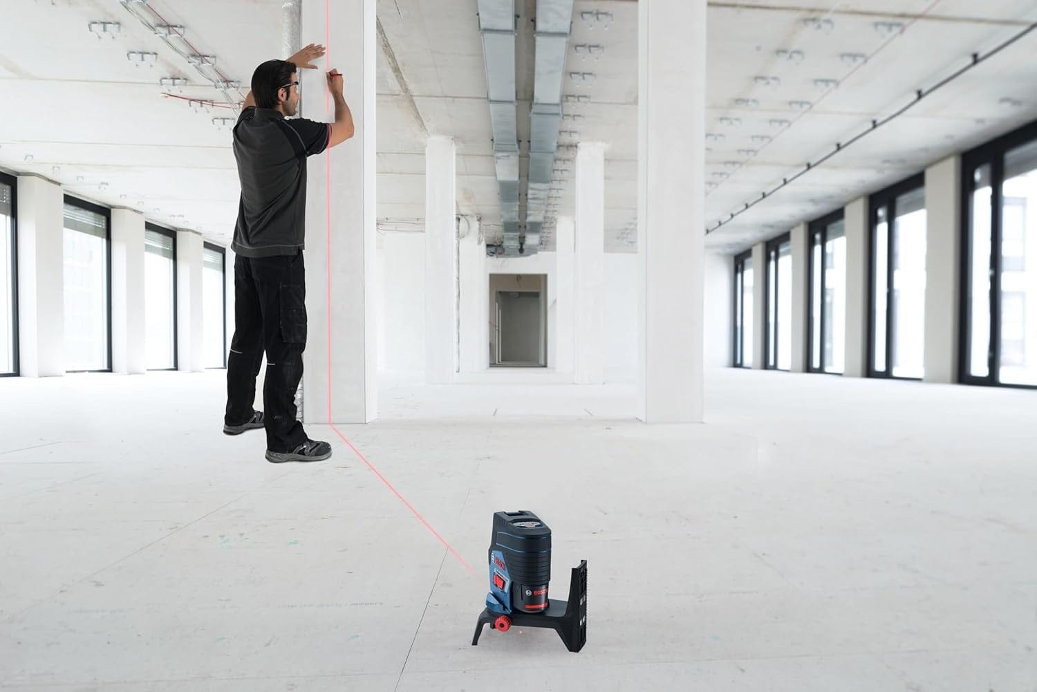 An action shot of a professional using the Bosch GCL100-80C-RT in a construction space, projecting a vertical red plumb line onto a column for precise alignment.