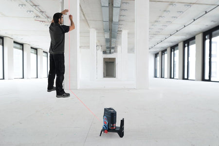 An action shot of a professional using the Bosch GCL100-80C-RT in a construction space, projecting a vertical red plumb line onto a column for precise alignment.