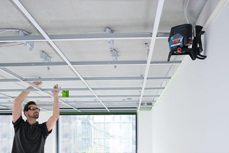 A worker installing a suspended ceiling grid, using the laser level mounted on a wall track to ensure perfect alignment of the metal frame.