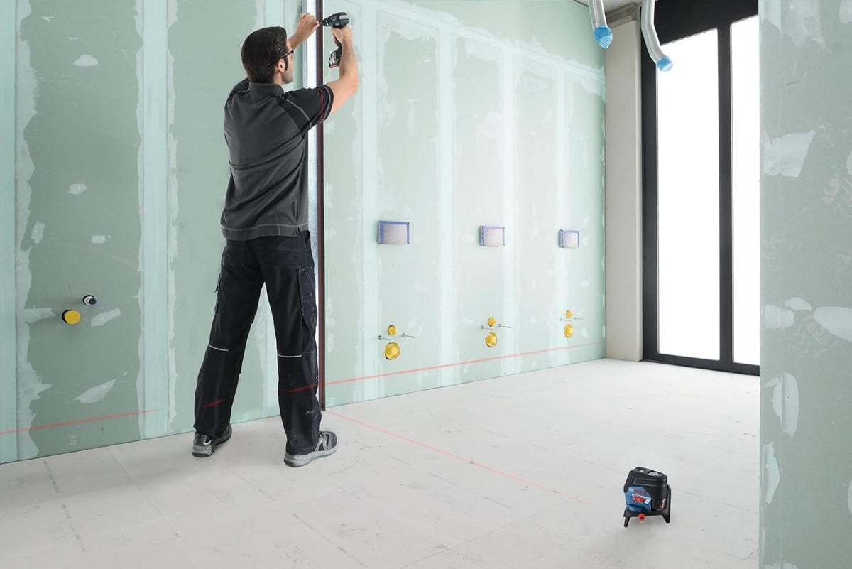 Contractor utilizing the Bosch GCL100-80C laser level on the floor to maintain plumb and level accuracy during the installation of metal track for drywall framing.