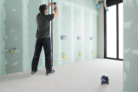 Contractor utilizing the Bosch GCL100-80C laser level on the floor to maintain plumb and level accuracy during the installation of metal track for drywall framing.
