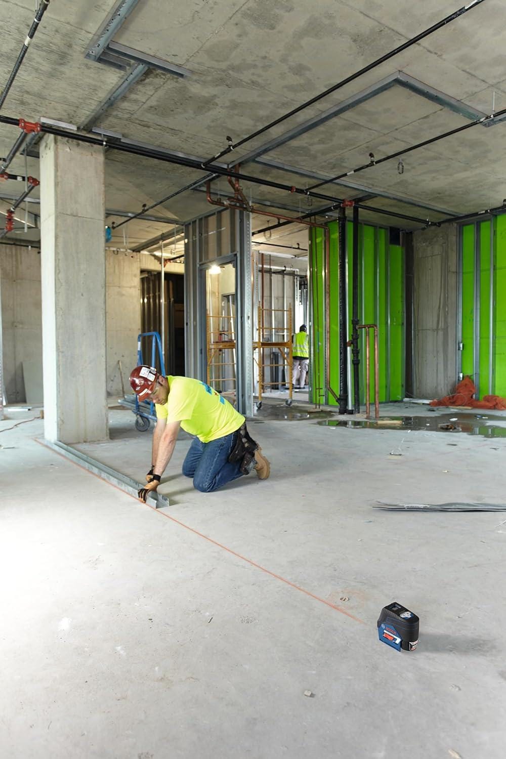 A worker aligning a floor track using the visible red line projected by the Bosch GCL100-80C 12V Max connected cross-line laser in a large open construction area.