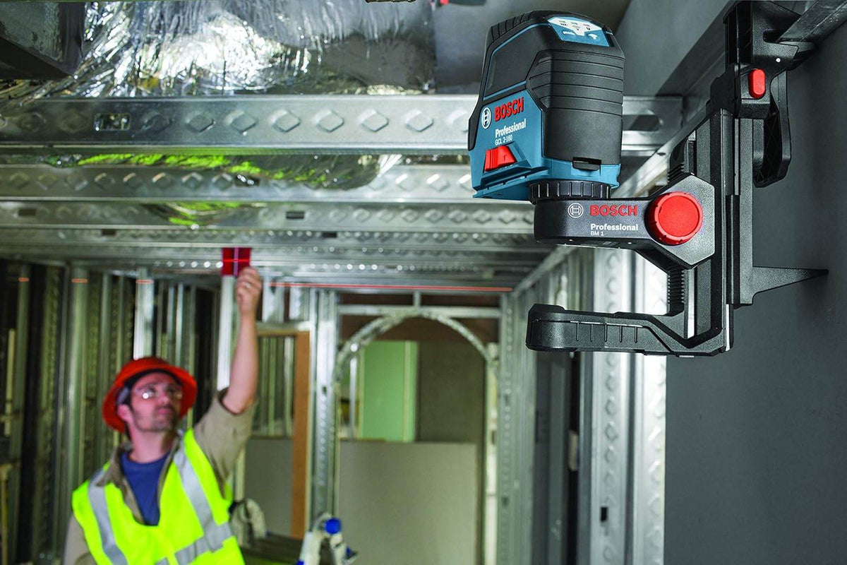 Bosch GCL 2-160 laser level clamped to metal beam projecting red vertical line; worker uses measuring stick for alignment under beam.