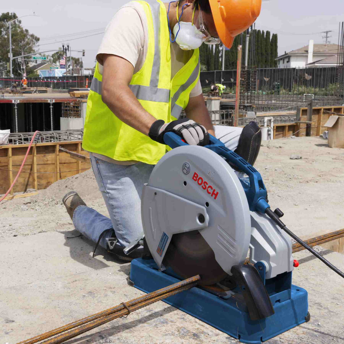 A construction worker kneeling on a concrete slab using the abrasive cut-off machine to slice through steel rebar.