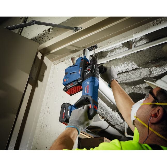 Person using a Bosch rotary hammer drill overhead near a doorway, wearing safety gear in an industrial setting.