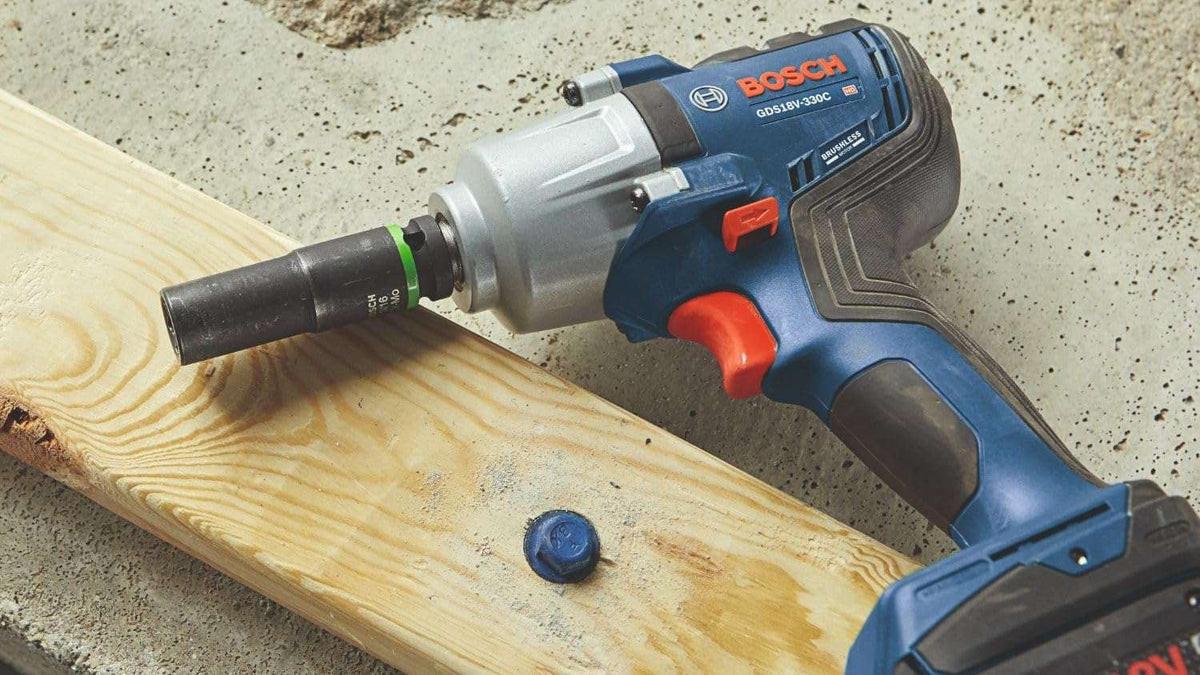 A high-angle product shot of the Bosch mid-torque impact wrench resting on a wooden board next to a blue heavy-duty bolt, showing an impact socket attached to the anvil.