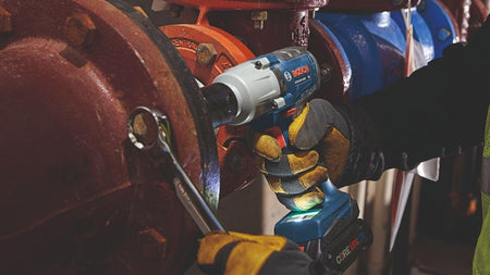 An action shot showing a professional using the Bosch impact wrench and a socket to tighten a large bolt on a heavy industrial red plumbing valve.