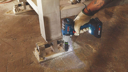 An action shot showing the Bosch impact wrench with an attached deep socket being used to secure a bolt into a metal structural beam on a construction site.