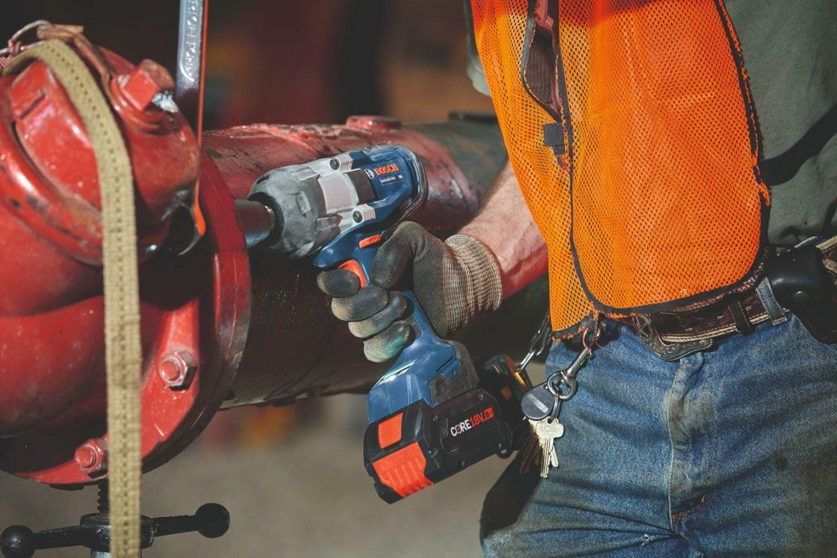 A professional technician using the Bosch 18V high-torque impact wrench with a CORE18V battery to fasten heavy-duty industrial pipe fittings on a jobsite.