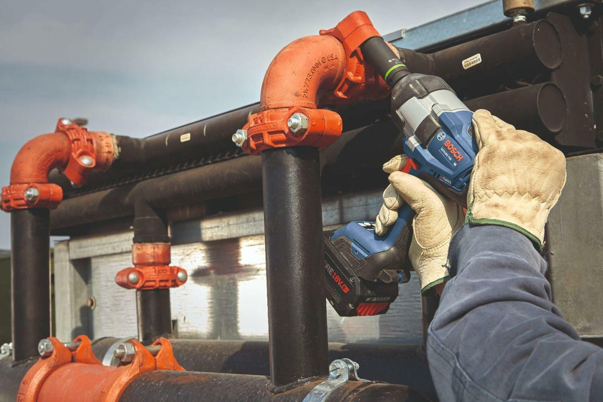 Close-up shot of a contractor in safety gloves using the Bosch BITURBO brushless impact wrench to secure large diameter bolts on an outdoor industrial plumbing manifold.