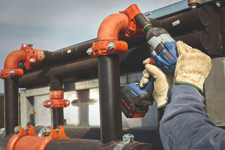 Close-up shot of a contractor in safety gloves using the Bosch BITURBO brushless impact wrench to secure large diameter bolts on an outdoor industrial plumbing manifold.