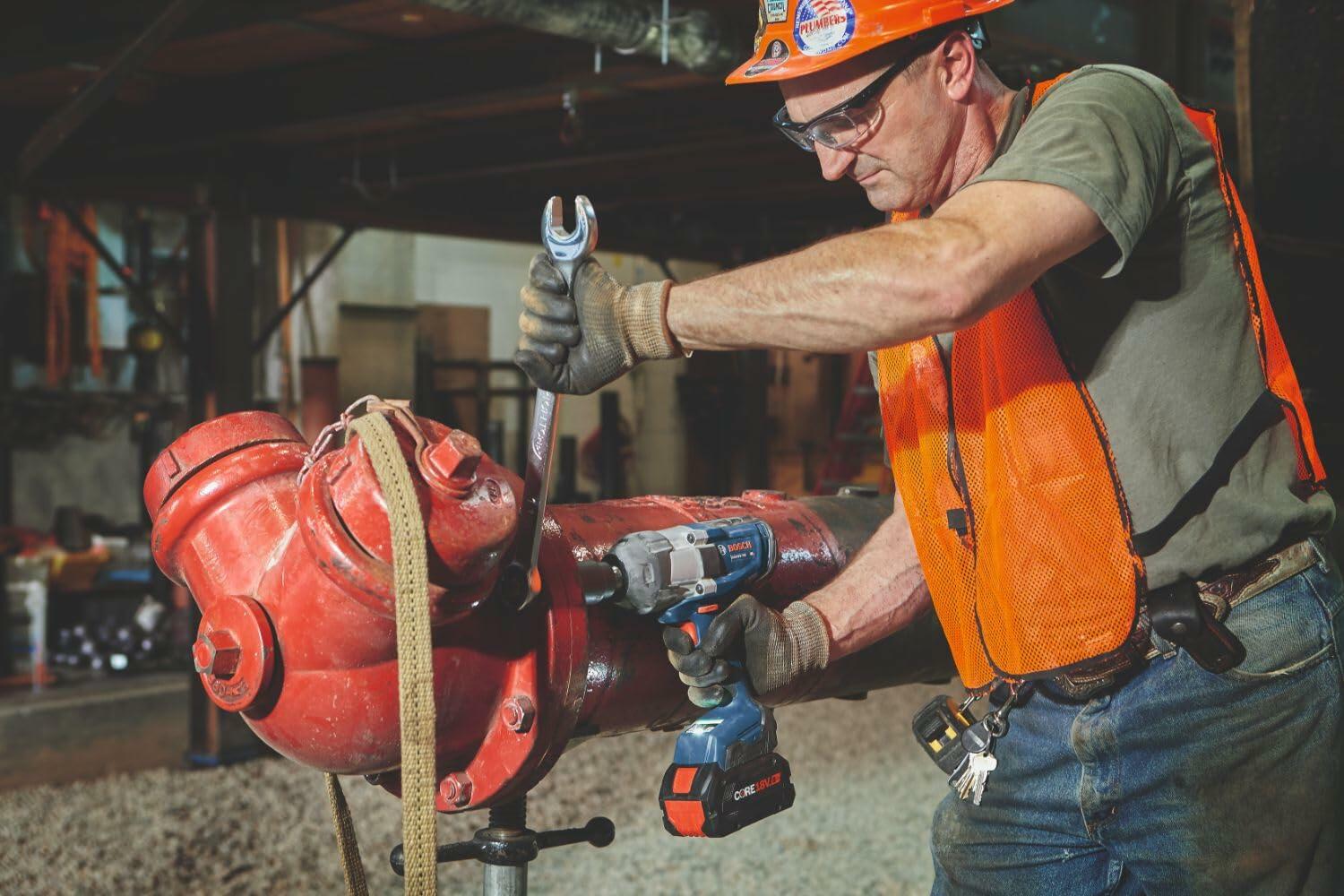 An electrician or plumber in high-visibility gear utilizing the Bosch PROFACTOR high-torque impact wrench and a manual wrench to tighten heavy-duty red pipe couplings.