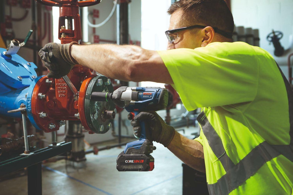 Action shot showing a maintenance worker using the Bosch GDS18V-740 impact wrench to service a large industrial valve assembly in a mechanical room.