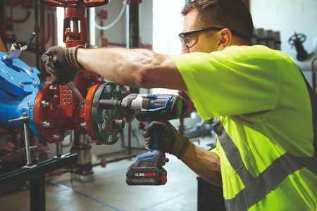 Action shot showing a maintenance worker using the Bosch GDS18V-740 impact wrench to service a large industrial valve assembly in a mechanical room.