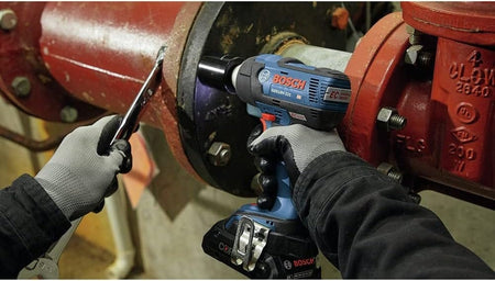 Close‑up of a Bosch GDS18V‑221 18V EC Brushless impact wrench being used alongside a manual wrench on a red industrial pipe flange, highlighting high‑torque fastening performance for mechanical, plumbing, and industrial maintenance applications.