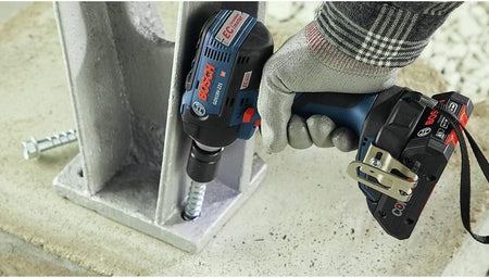 Worker using a Bosch GSB18V‑21 cordless drill to drive a heavy‑duty screw through a metal base plate into concrete, demonstrating powerful fastening capability and CORE18V battery performance for structural installation tasks.