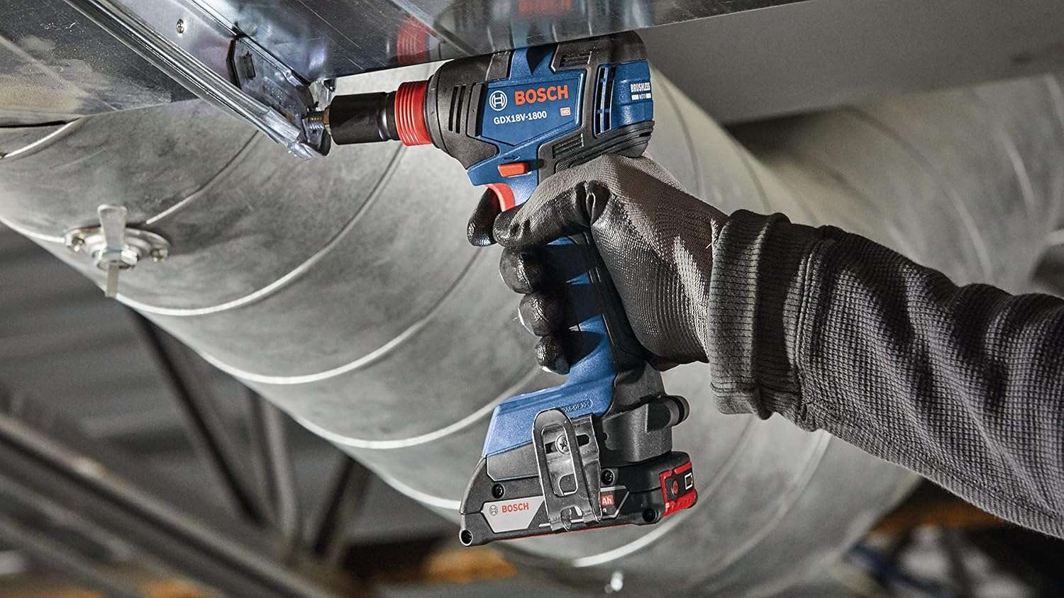 Close-up action shot showing a person wearing a protective glove using the Bosch impact tool as a driver to fasten a screw into a metal HVAC duct connection.