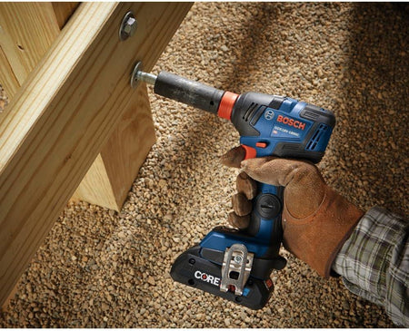 An action shot of a worker using the hybrid impact tool with a socket to drive a large bolt into a heavy-duty wooden structural beam outdoors.