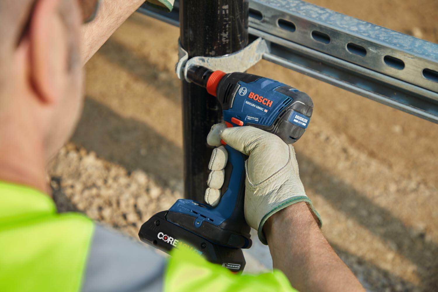 A worker wearing leather gloves uses the Bosch GDX18V-1860CN impact driver (with an attached battery) to fasten a clamp onto a metal pipe railing on a construction site.