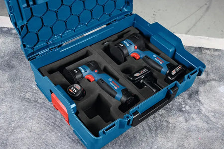 An open Bosch L-Boxx system hard carrying case lined with a custom-cut dark foam insert organizer tray. Nestled securely inside the protective foam compartments are the Bosch 12V random orbital sander bare tool, a compact matching 12V handheld polisher, two attached rechargeable lithium-ion battery packs, and a standalone 12V max power cell ready for mobile auto detailing tasks.
