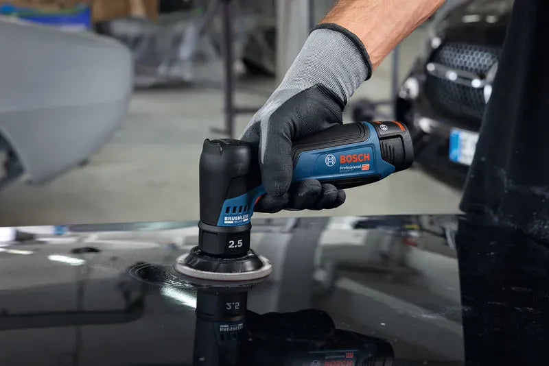 An automotive body technician wearing gray and black protective work gloves using the Bosch GEX12V-77N 12V Max random orbital sander to complete wet or dry finishing on a dark car hood. The tool's compact size allows for focused surface leveling on localized spot paint repairs.