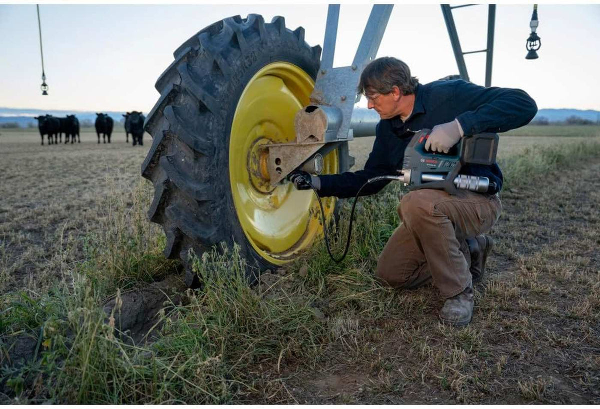 A wide outdoor shot of a technician servicing a center-pivot irrigation system in a farm field using the Bosch 18V grease gun, illustrating the tool's versatility for remote heavy equipment maintenance.