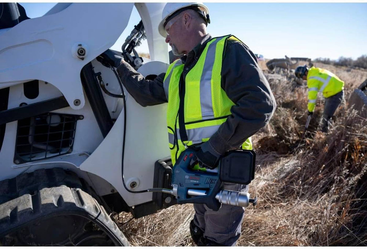 An operator wearing a safety vest and hard hat uses the Bosch GFP18V-10N with the included shoulder strap to lubricate the pivot points of a white compact track loader on a job site.