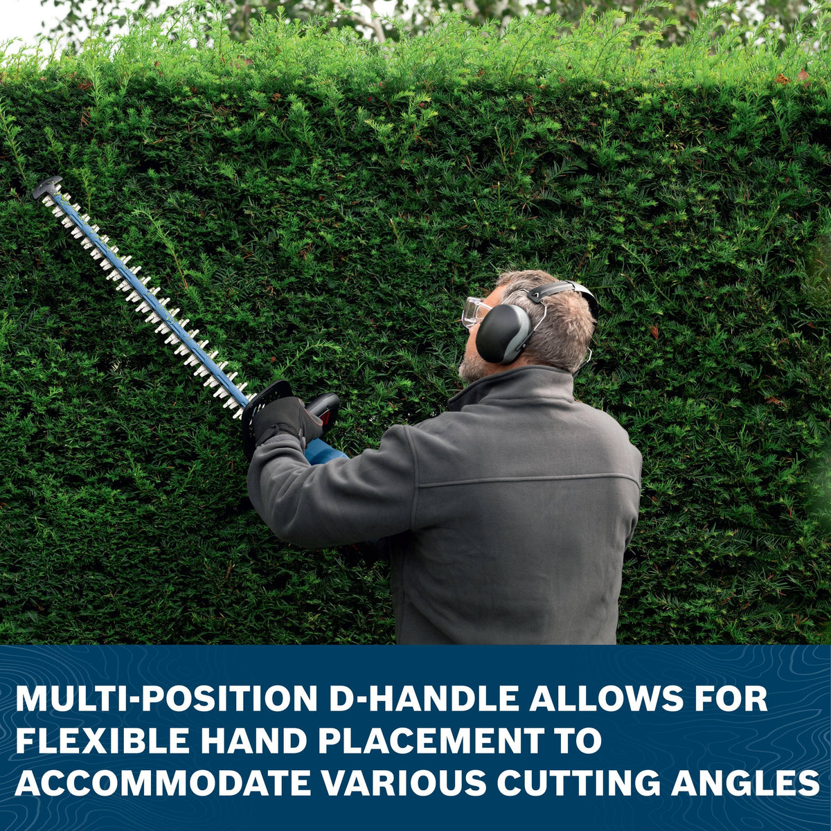 An application shot of an outdoor property manager wearing protective safety glasses and earmuffs holding the lightweight Bosch trimmer overhead to level off the flat top surface of a tall, manicured privacy hedge wall, positioned above a dark blue footer banner reading MULTI-POSITION D-HANDLE ALLOWS FOR FLEXIBLE HAND PLACEMENT TO ACCOMMODATE VARIOUS CUTTING ANGLES.