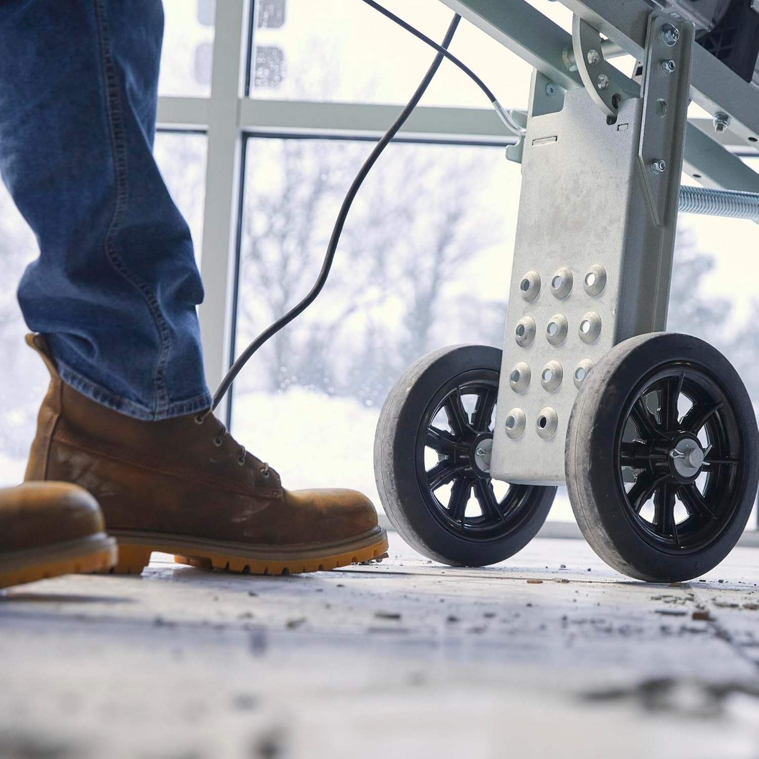 Low-angle shot focusing on the large, sturdy black rubber wheels of the cart as a worker maneuvers it across a debris-covered floor.